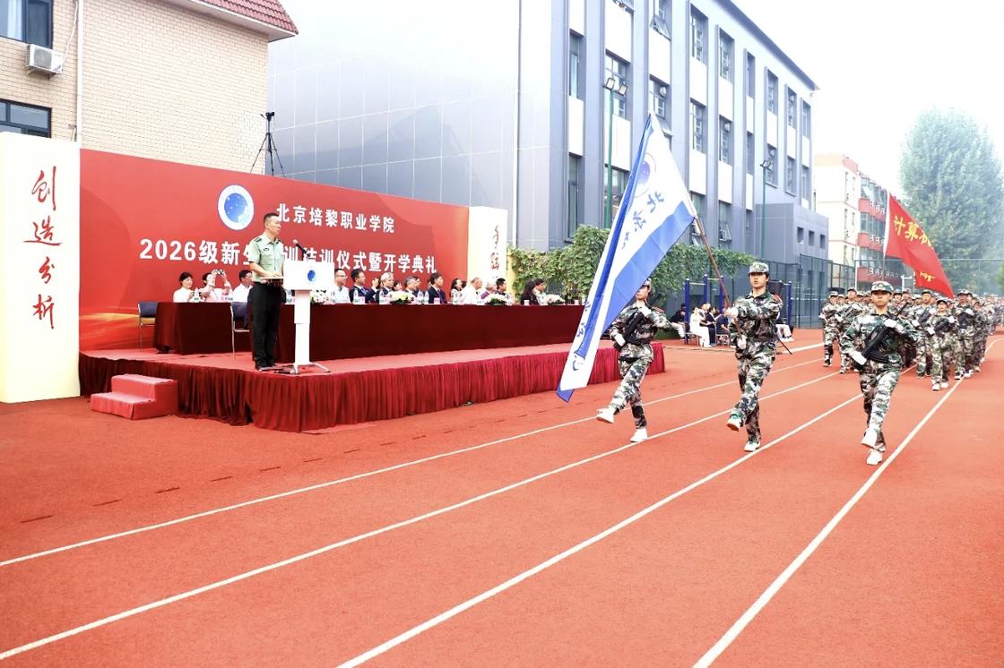 照片：军训结训仪式暨开学典礼——护旗手与持系旗的方队经过主席台，背景板印有仪式全称，各系旗帜随队列展开（学院官方微信文章配图，2026-09-19 收录）