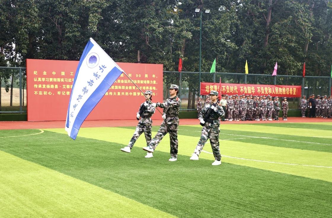 照片：军训结训仪式现场——护旗队员高擎旗帜齐步行进，身后红色主题展板印有「纪念中国工农红军长征胜利90周年」「传承发扬路易·艾黎职业教育思想」等字样，另一横幅写有「培黎青年 不负时代 不负韶华 不负党和人民的殷切希望」（学院官方微信文章配图，2026-09-19 收录）