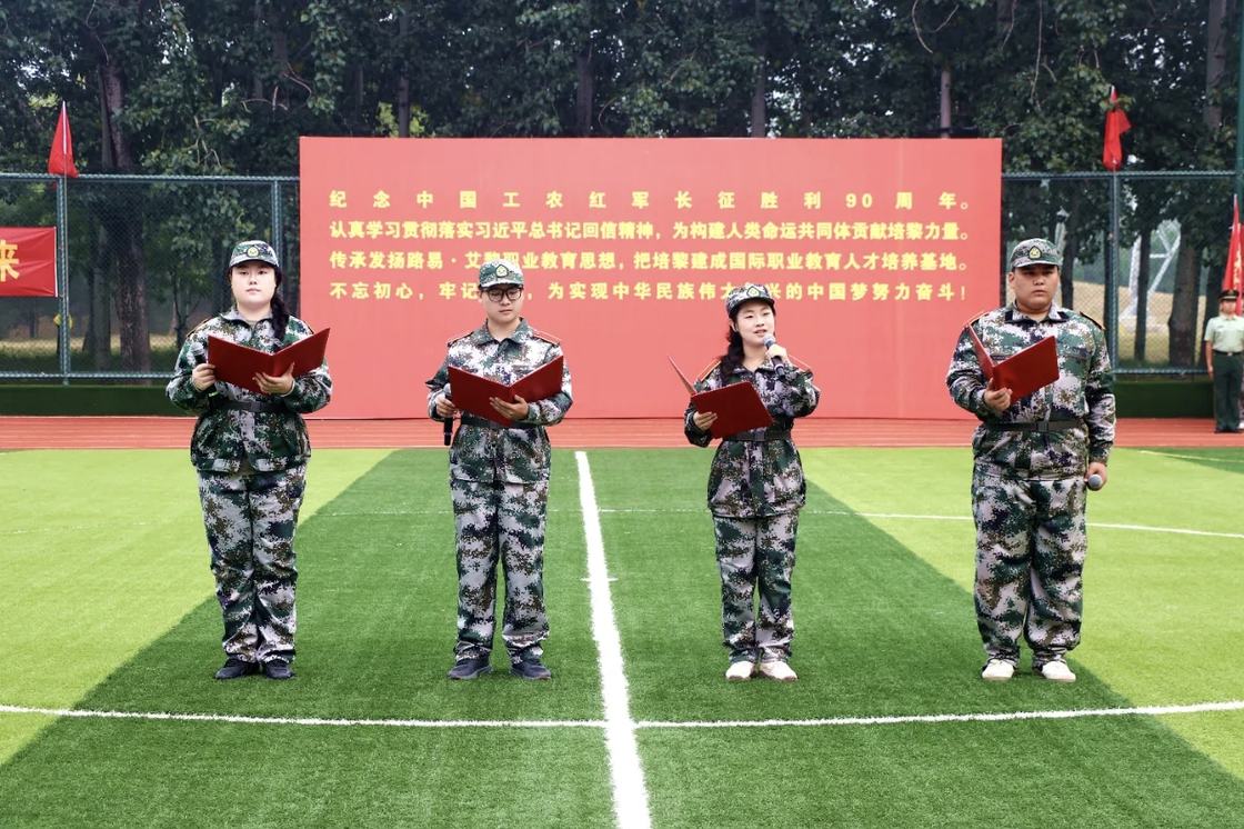 照片：军训结训仪式暨开学典礼集体朗诵环节——四名新生手持红色文件夹在球场朗诵，背景红色主题展板印有「纪念中国工农红军长征胜利90周年」等字样（学院官方微信文章配图，2026-09-19 收录）
